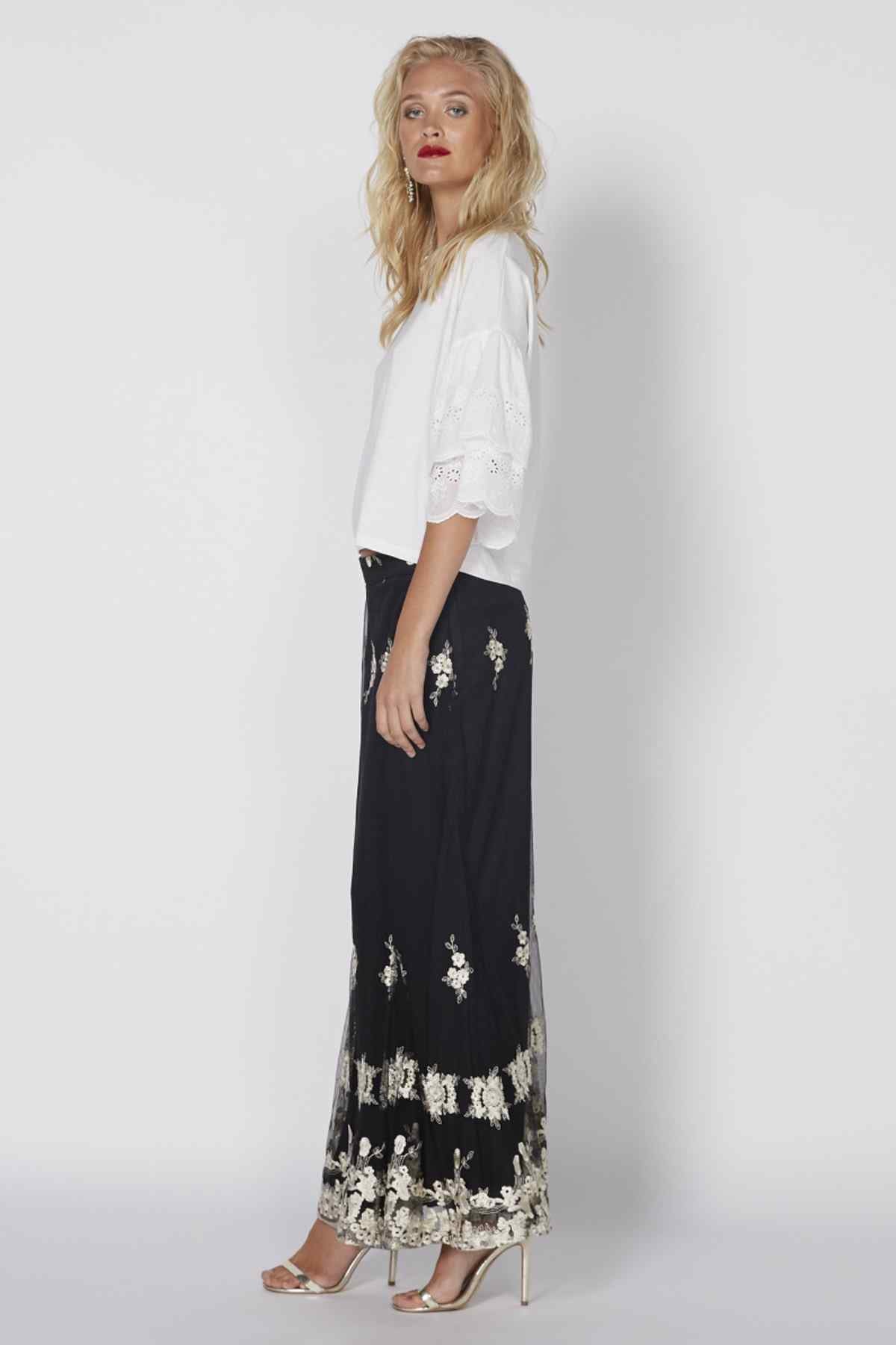 White eyelet blouse with short sleeves and scalloped hem, worn with dark embroidered skirt