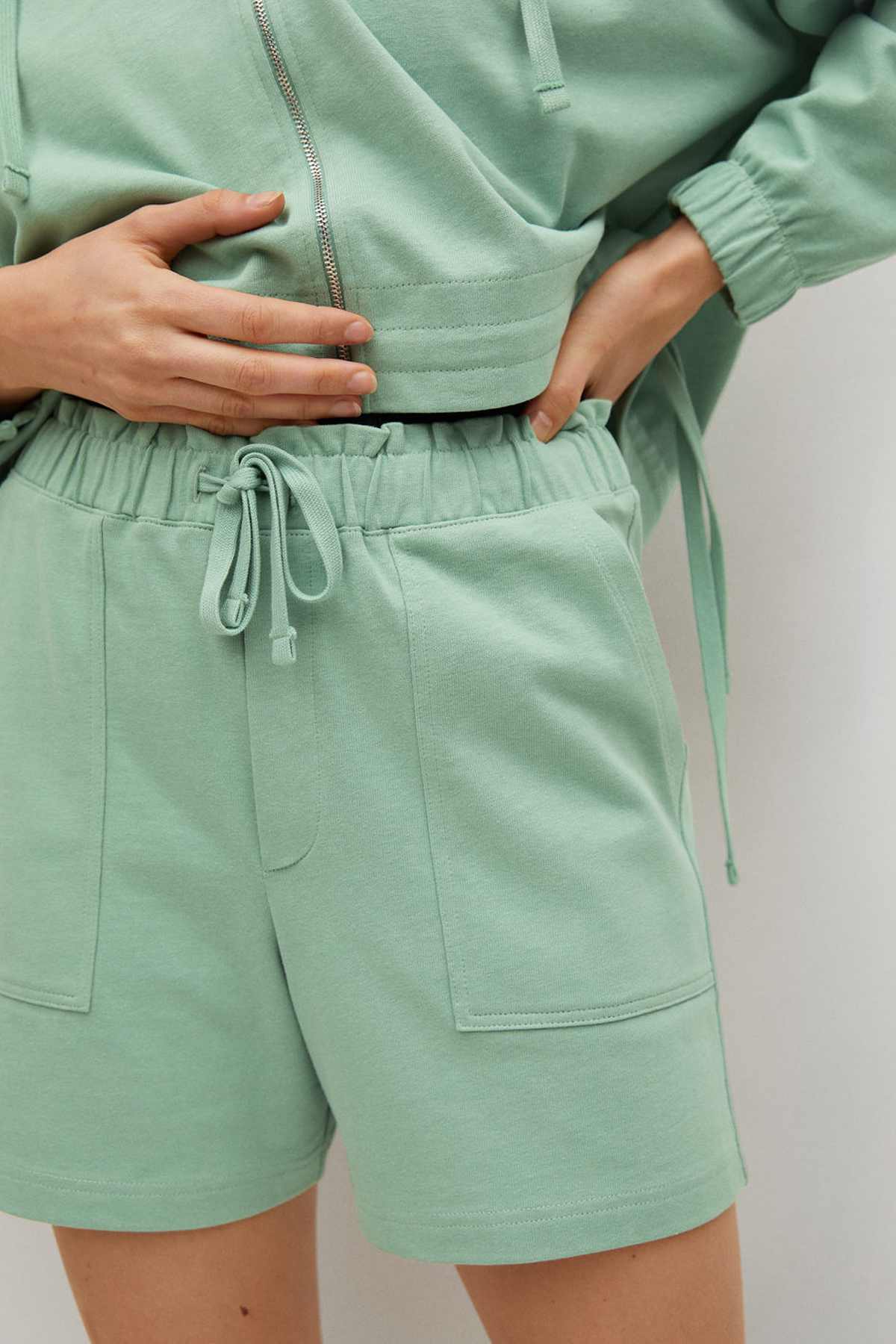 Pastel green hoodie hem and drawstring shorts with side pockets, close-up