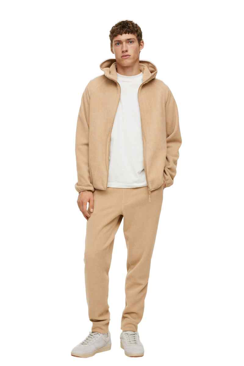 Beige zip-up hoodie with drawstring hood and beige jogger pants, white sneakers.
