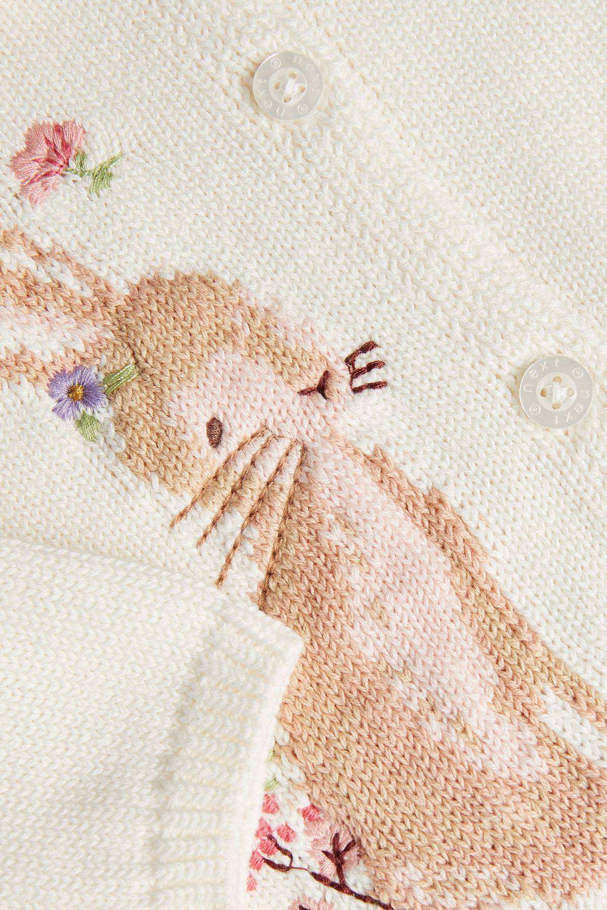 Cream knit sweater close-up: bunny face illustration, flowers, and button detail