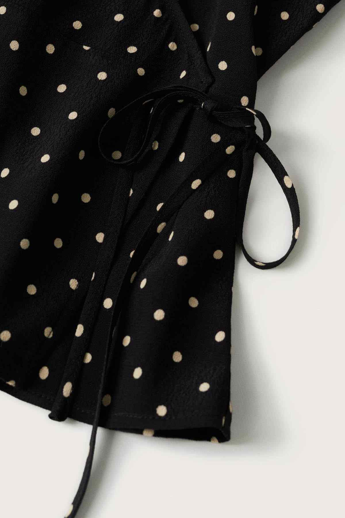 Black polka-dot blouse close-up with tied drawstring waist and gathered sleeve cuff.