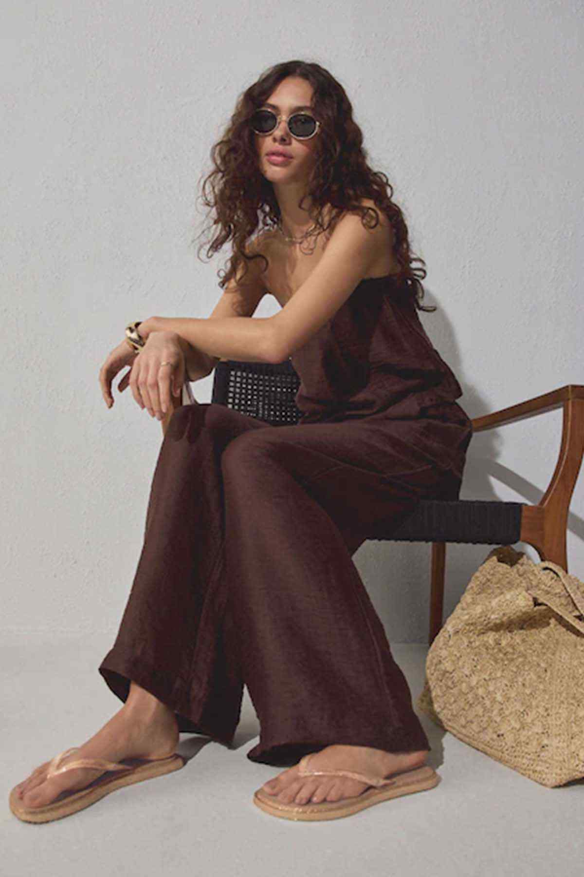 Dark brown wide-leg jumpsuit with rose-gold thong sandals, seated