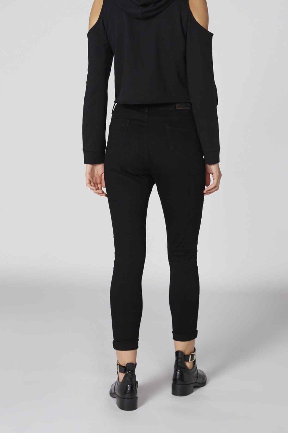 Black skinny jeans with cuffed hem and cold-shoulder cropped jacket from behind