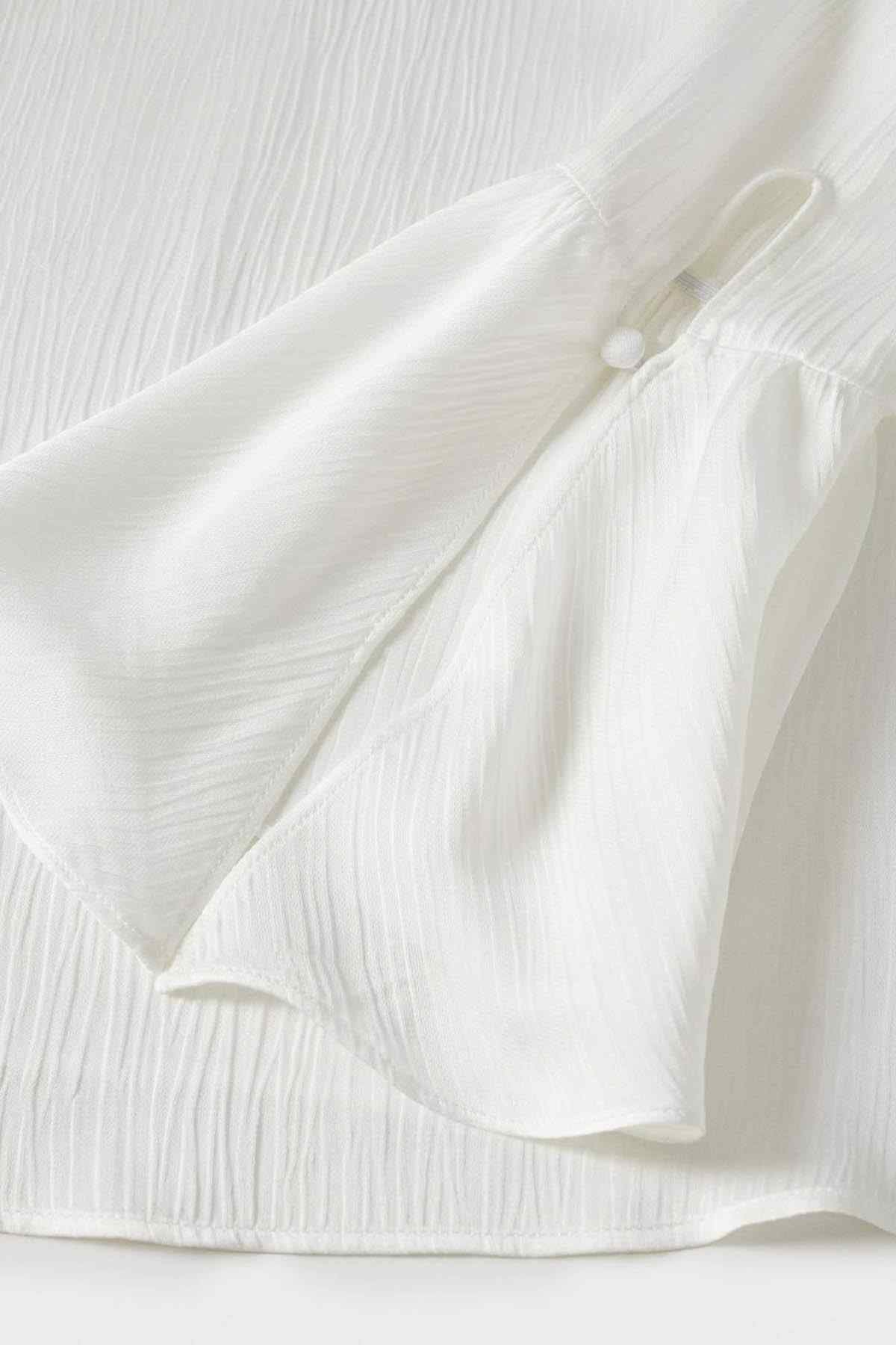 Off-white textured blouse fabric with gathered sleeve cuffs and small button placket.