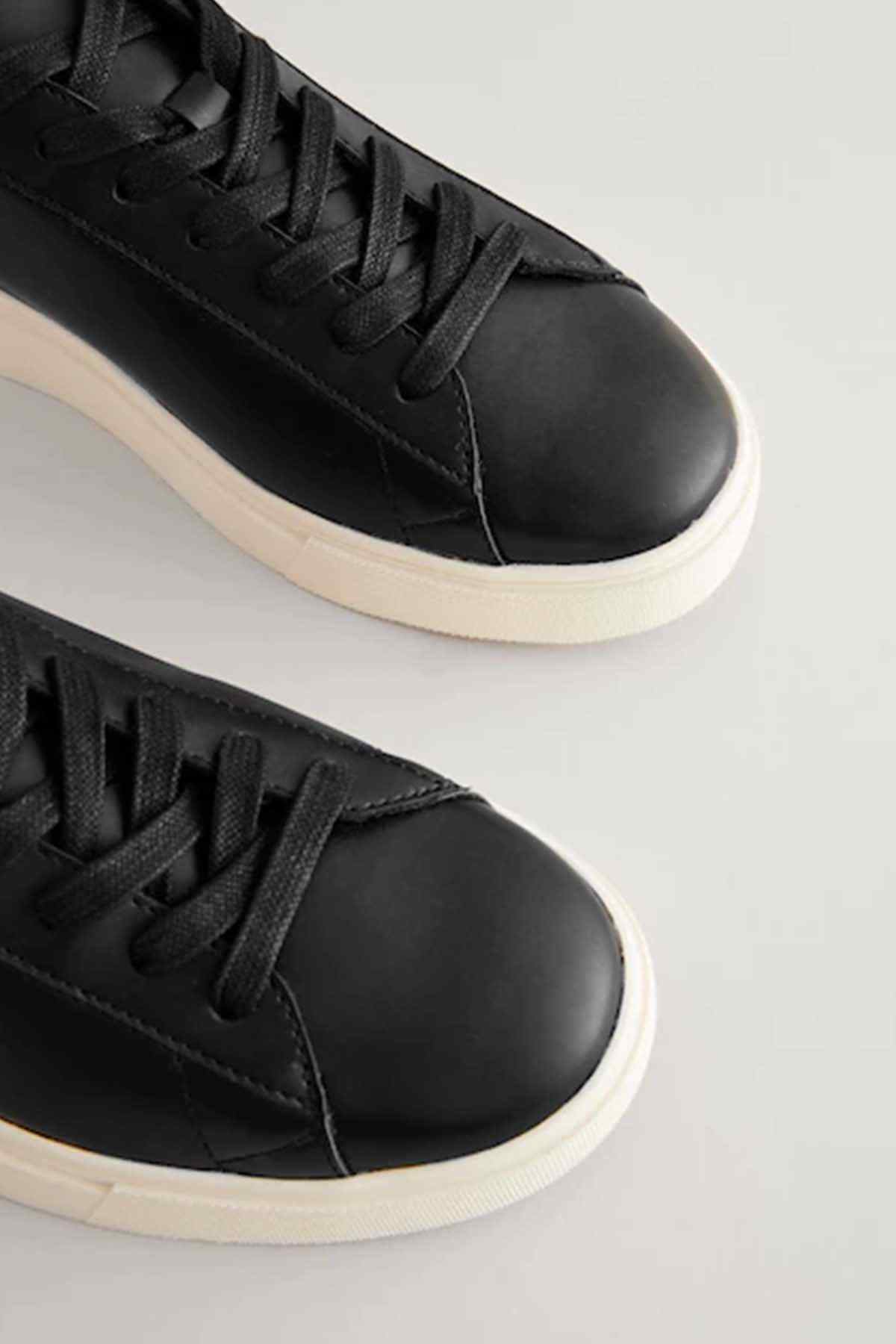 Black lace-up sneakers close-up, black uppers with textured stitching and white sole