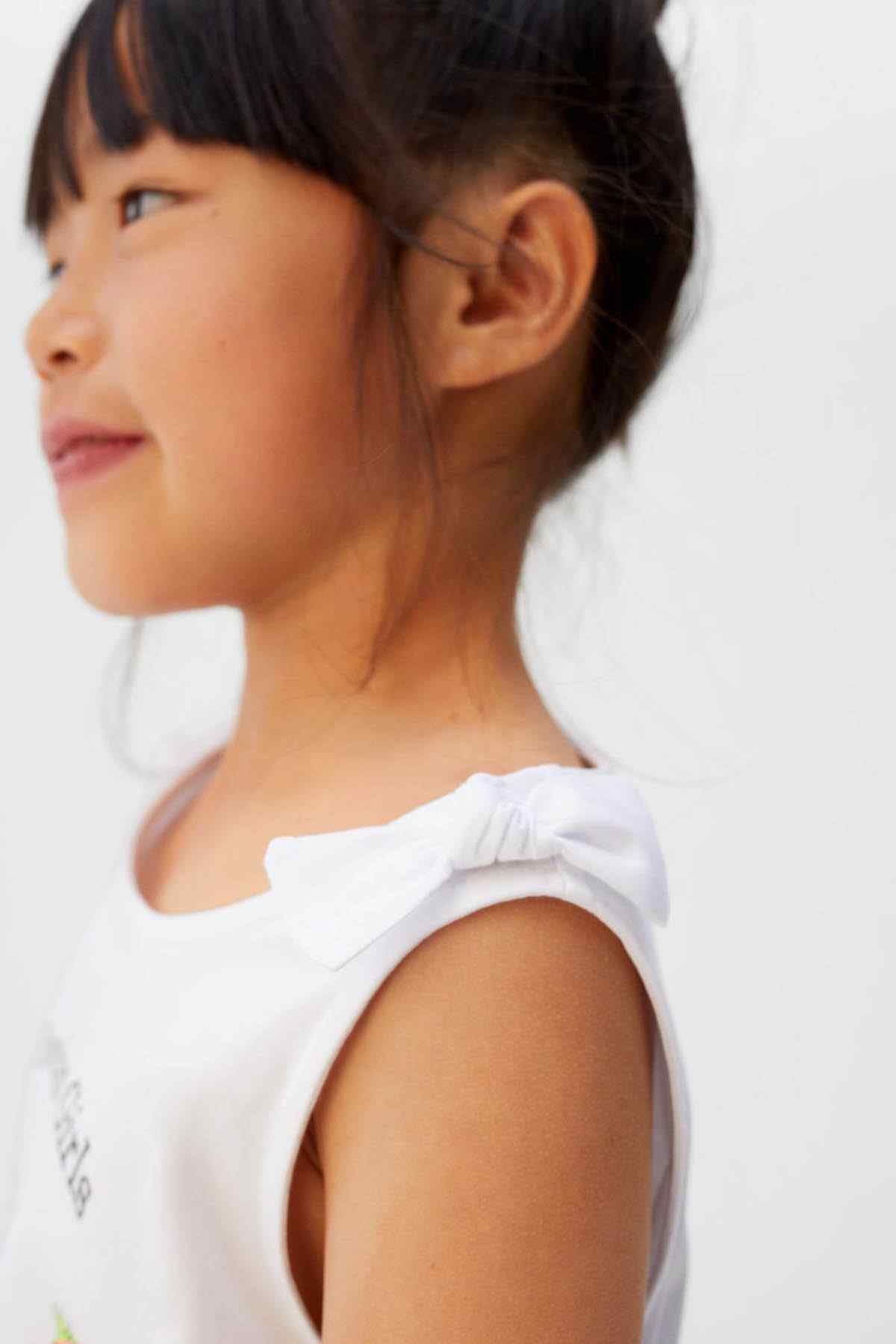 Off-white girls' sleeveless tank top with ruffled shoulder detail, side view