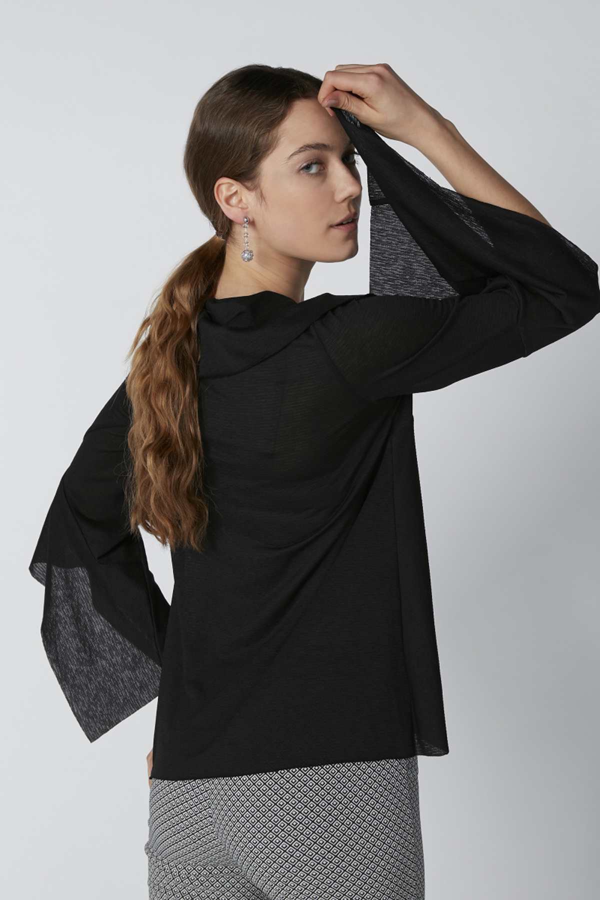 Black draped tunic top with wide sleeves and curved hem, styled over leggings