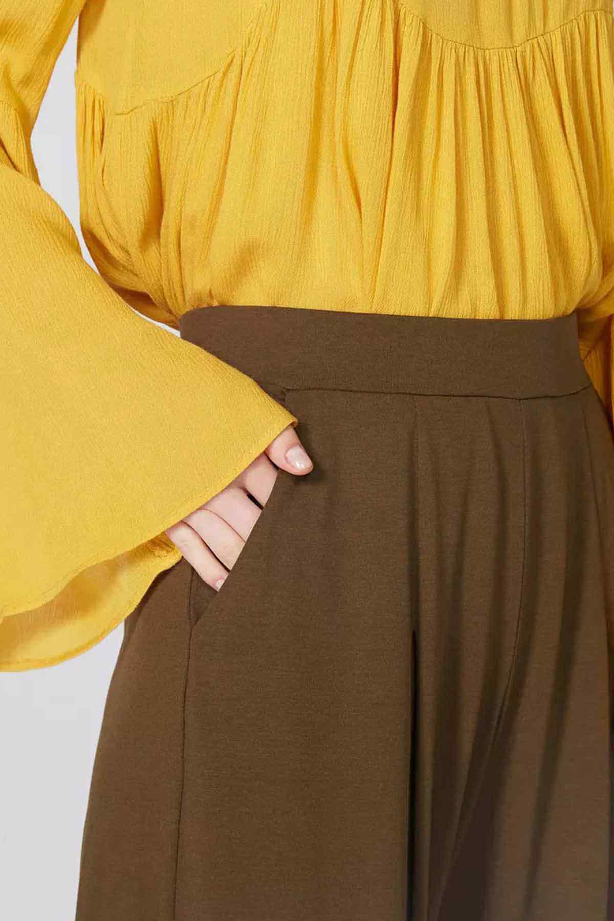 Yellow blouse tucked into brown high-waist wide-leg pants, side close-up