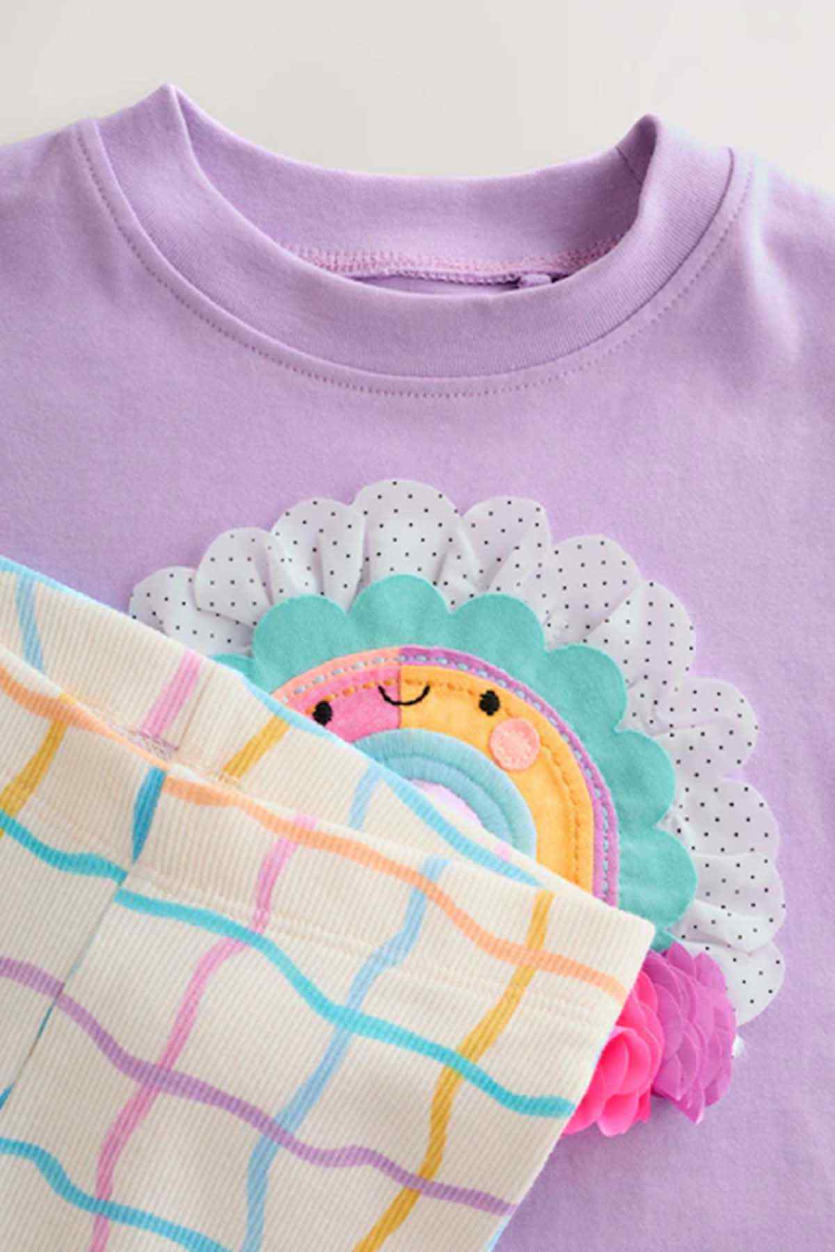 Close-up of lilac T-shirt hem with rainbow applique and white leggings with colorful grid print