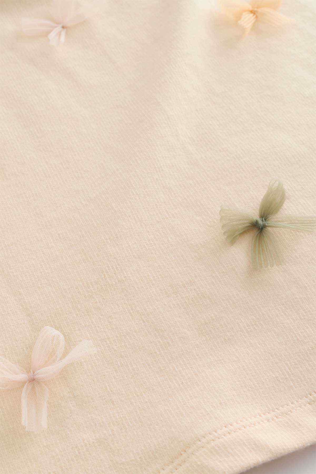 Ecru T-shirt fabric close-up with embroidered butterfly accents