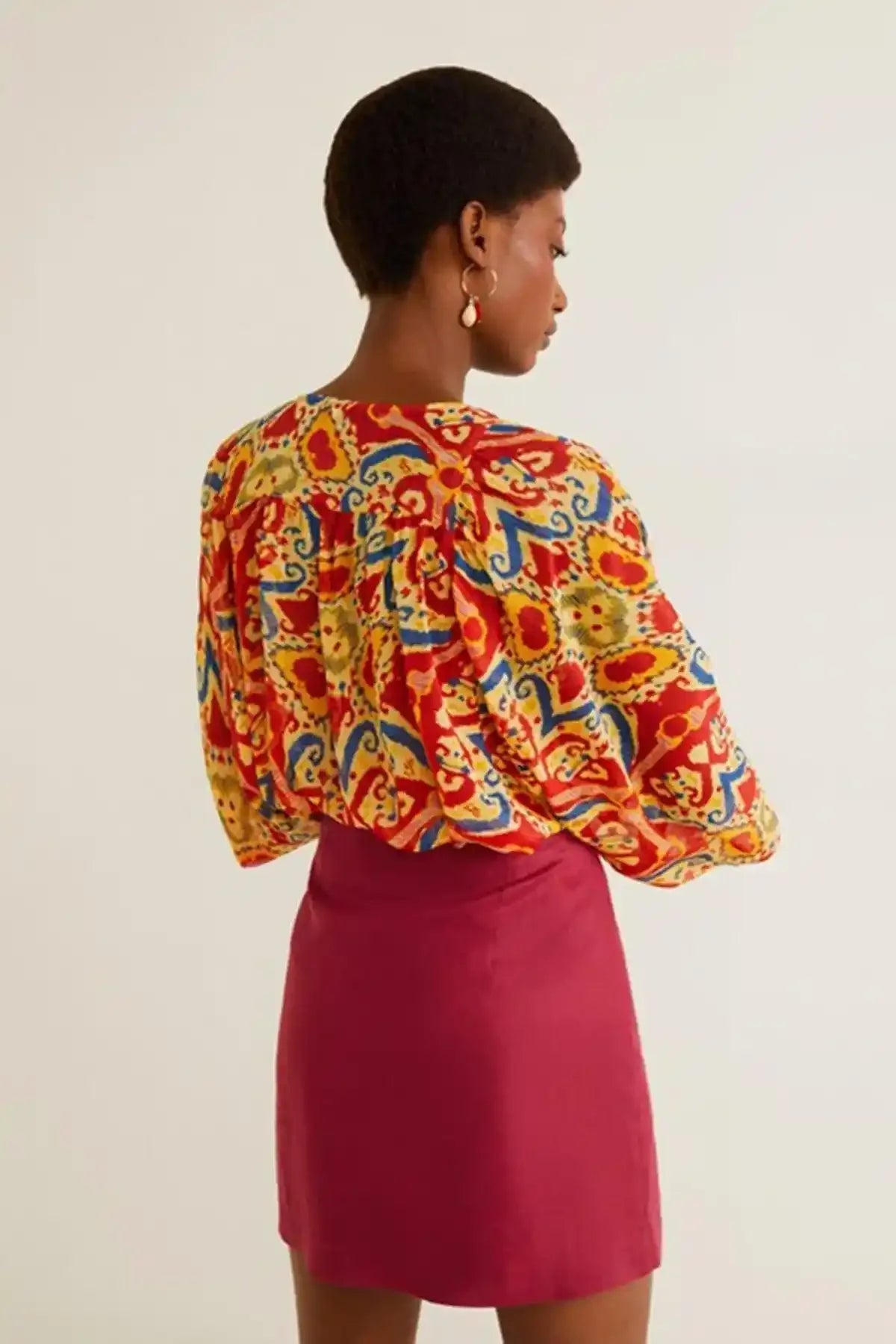 Back view of multicolor patterned blouse with gathered shoulders, worn with red mini skirt