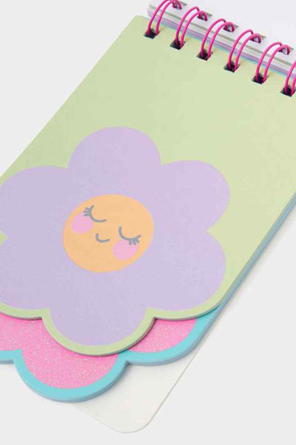 Pastel flower spiral notebook corner with closed-eye face illustration, glitter cover