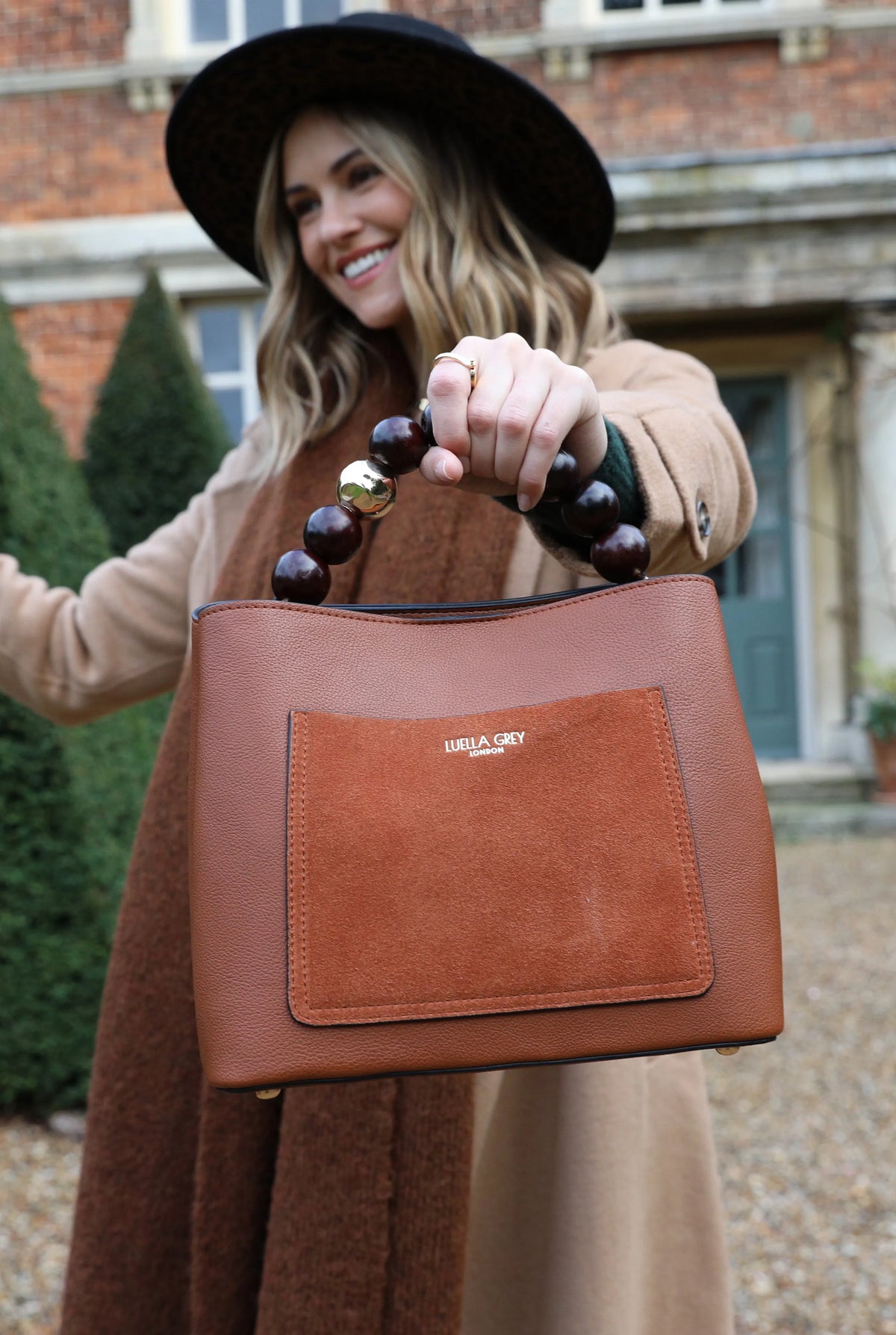 Brown leather handbag with beaded handle and front patch pocket, held outdoors.