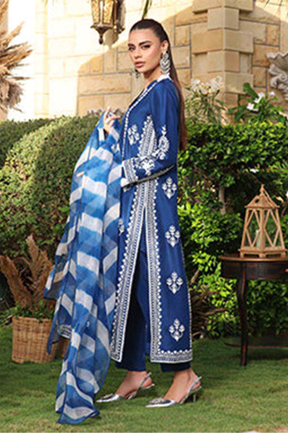 Blue embroidered long dress with white motifs and check dupatta, standing side view
