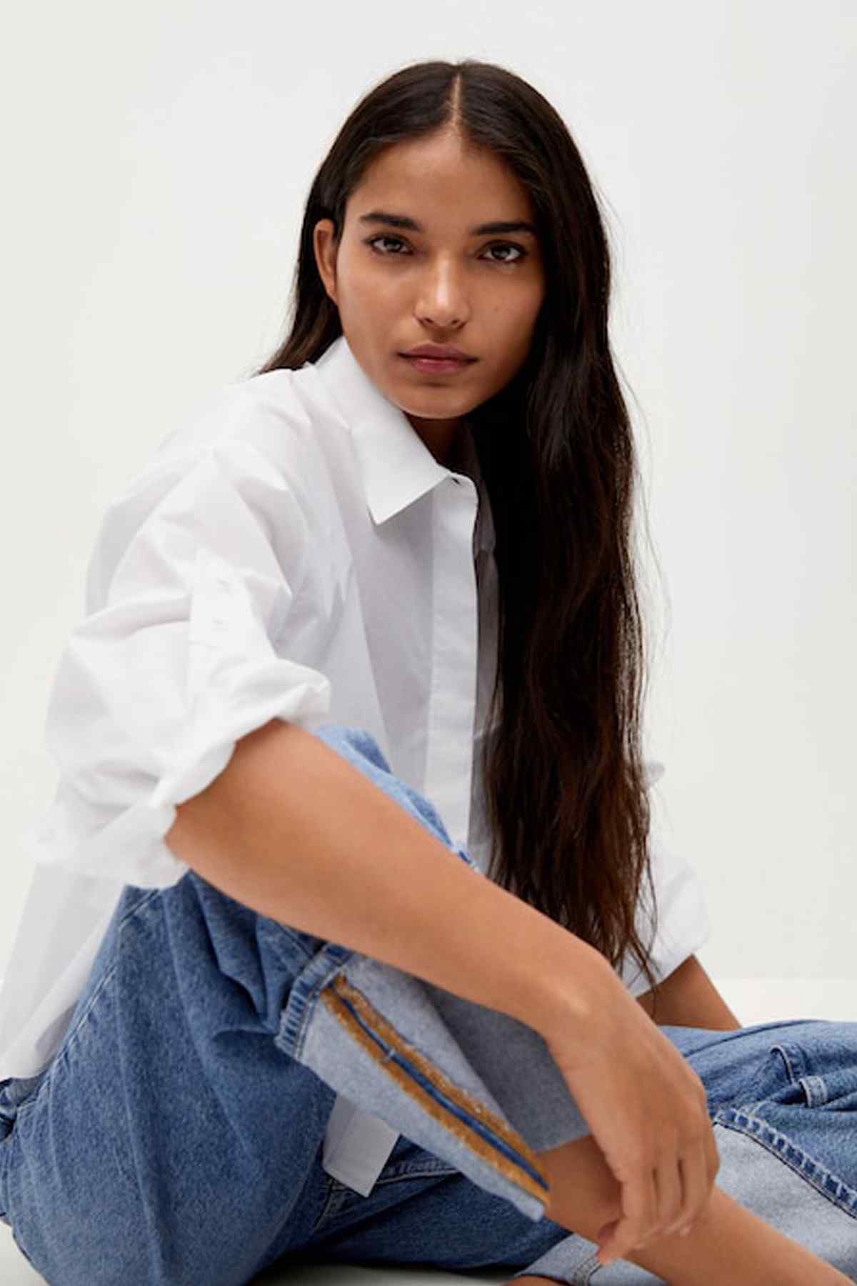 Off-white collared button-up shirt with loose sleeves, worn over blue denim