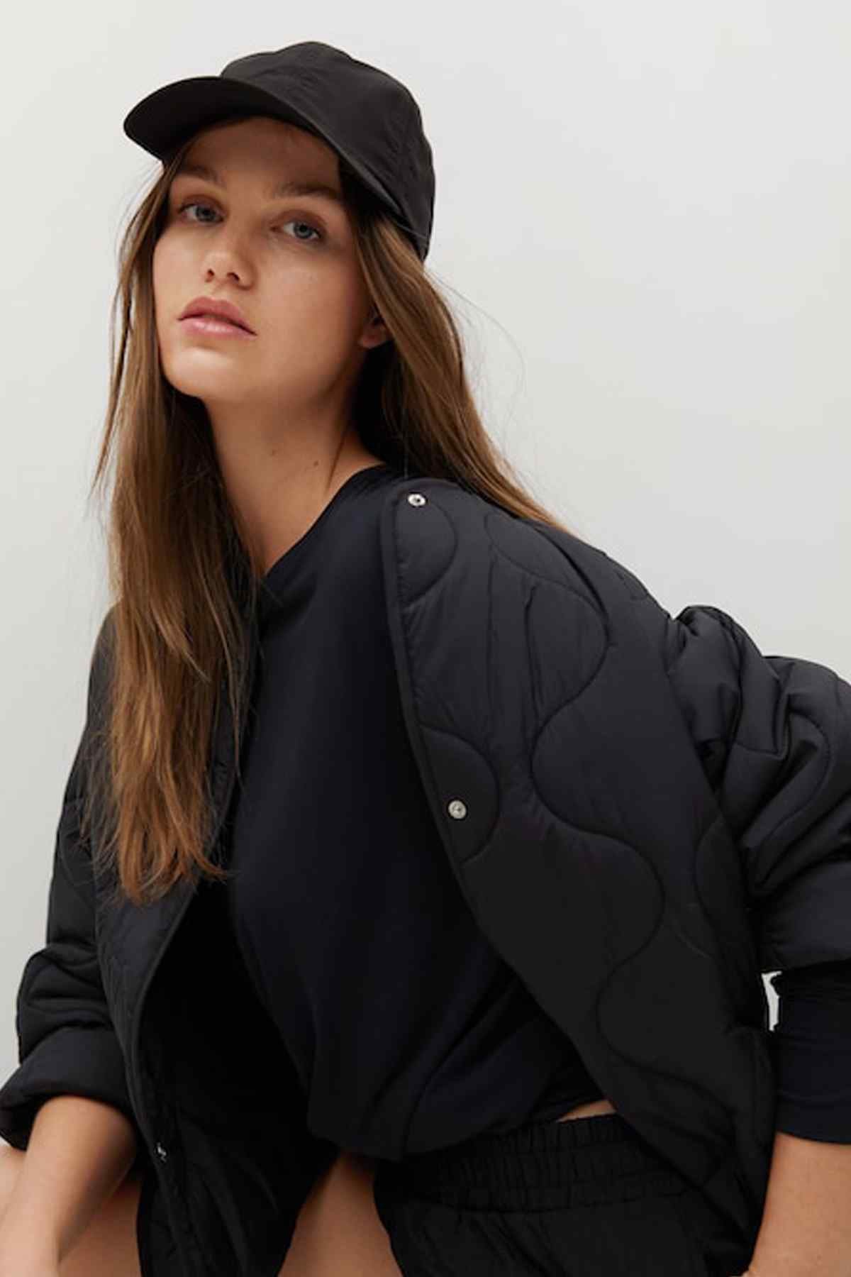 Black quilted jacket over long-sleeve top, with snap buttons, baseball cap