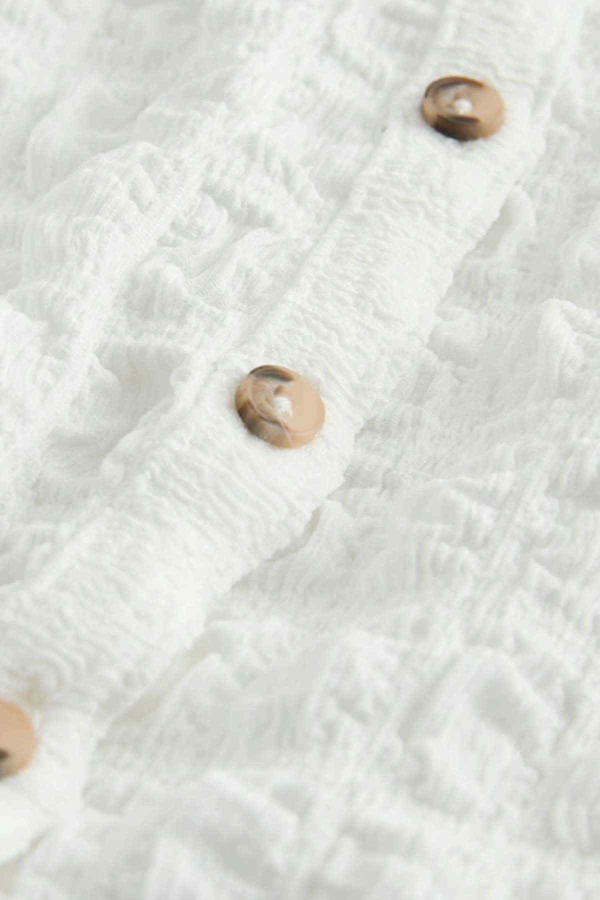 Close-up of white textured vest fabric with brown snap buttons