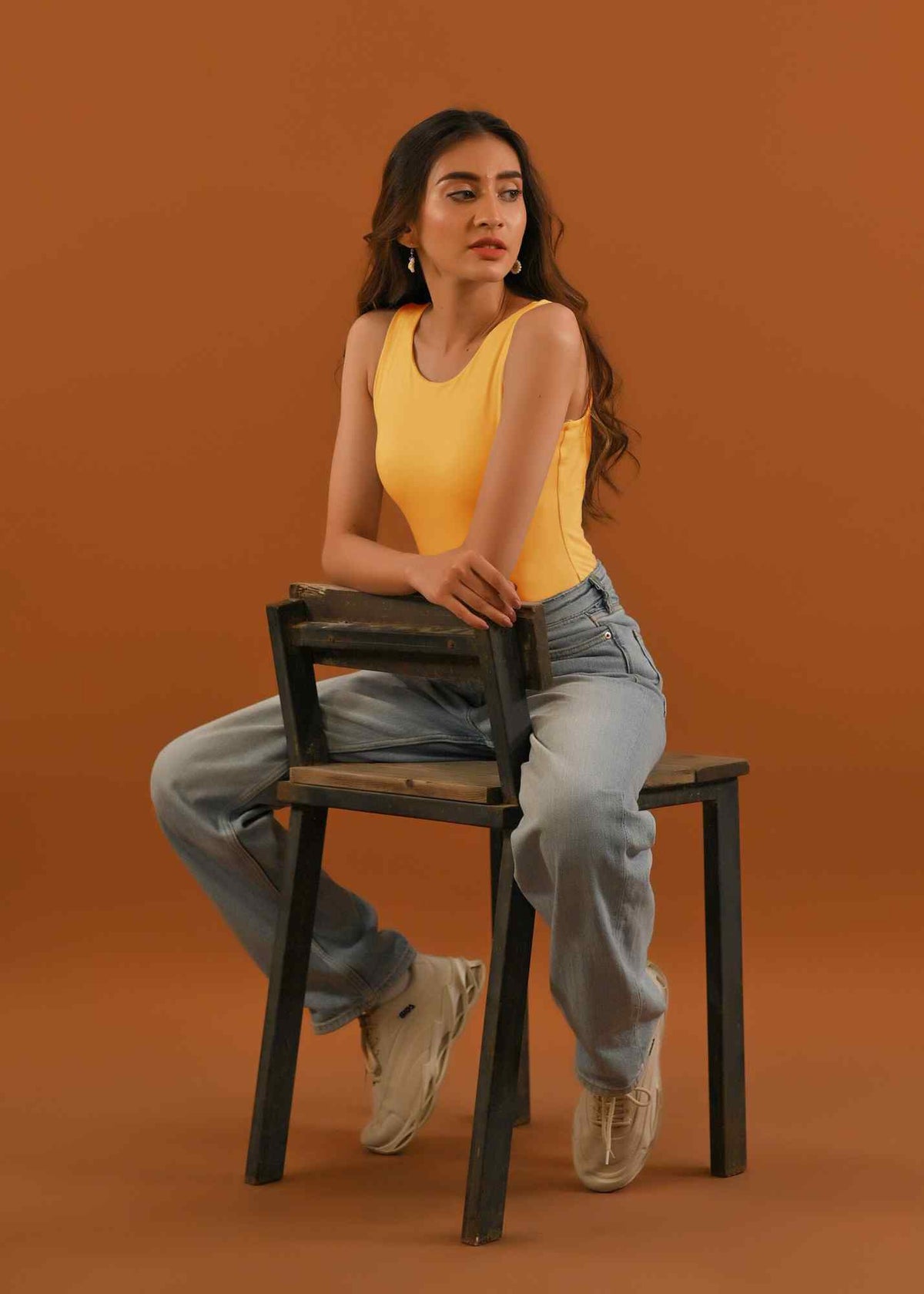Dhaga yellow tank top and light-wash jeans with button fly, seated pose