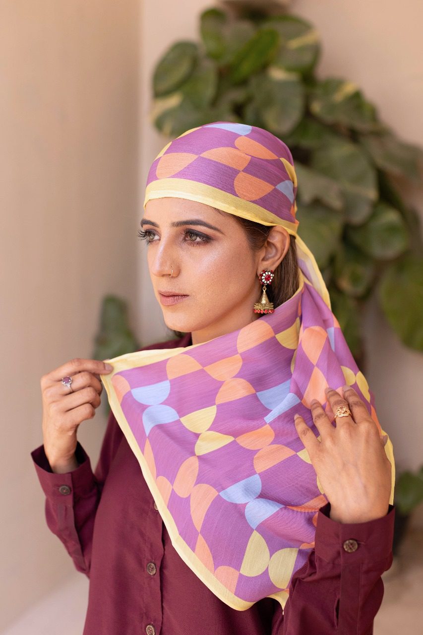 Purple patterned headscarf with yellow accents, draped over shoulders and tied back