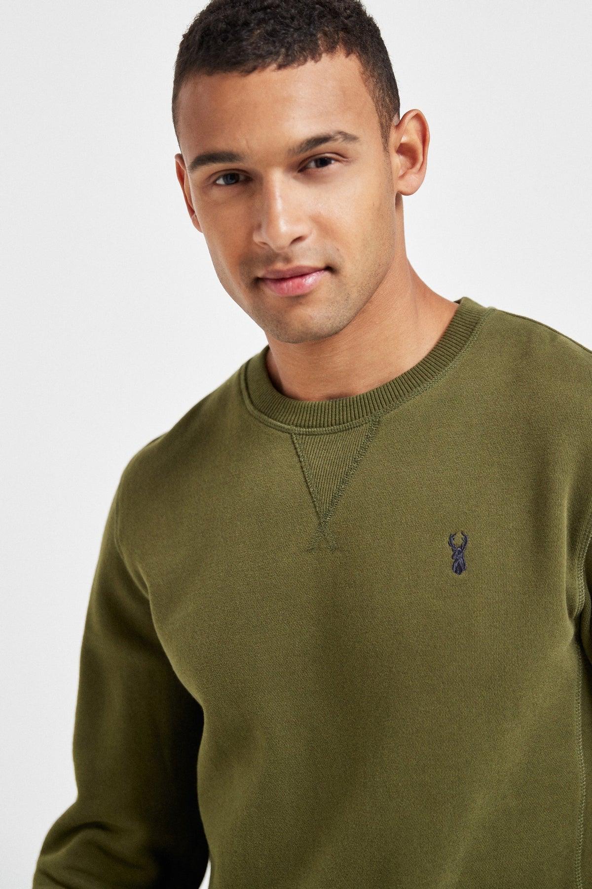 Olive green crewneck sweatshirt close-up, blue chest logo detail