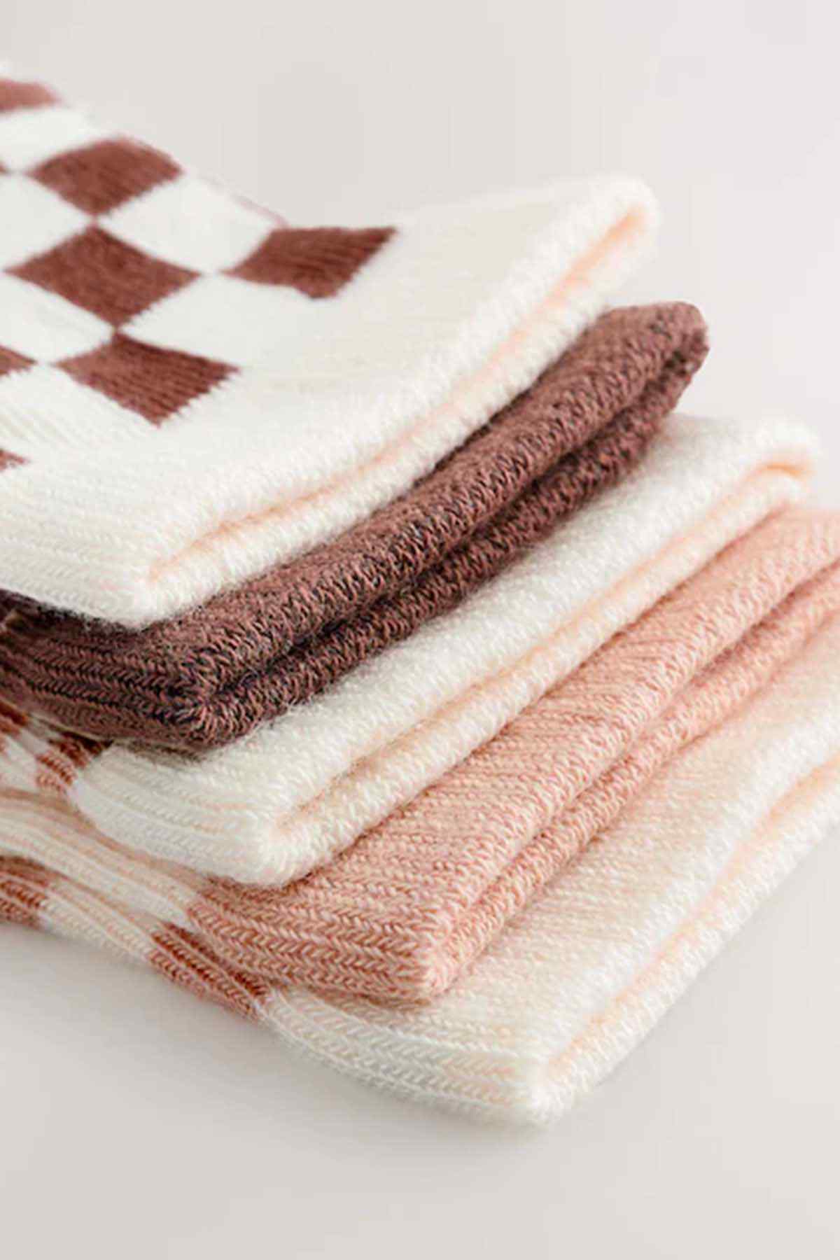 Stack of baby socks in cream, peach, and brown with check and animal prints