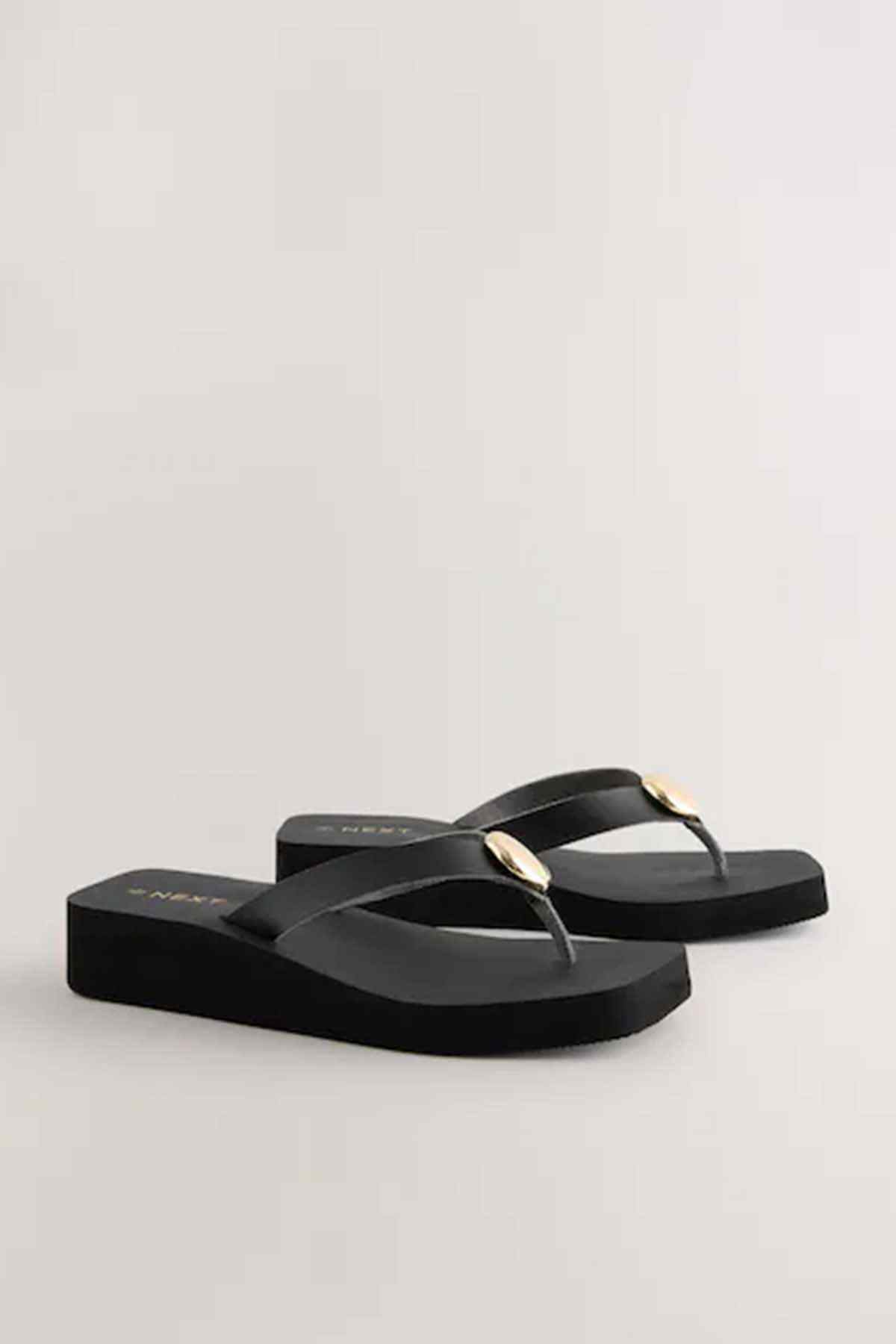 Pair of black flip-flop sandals with gold round buckle and flat sole