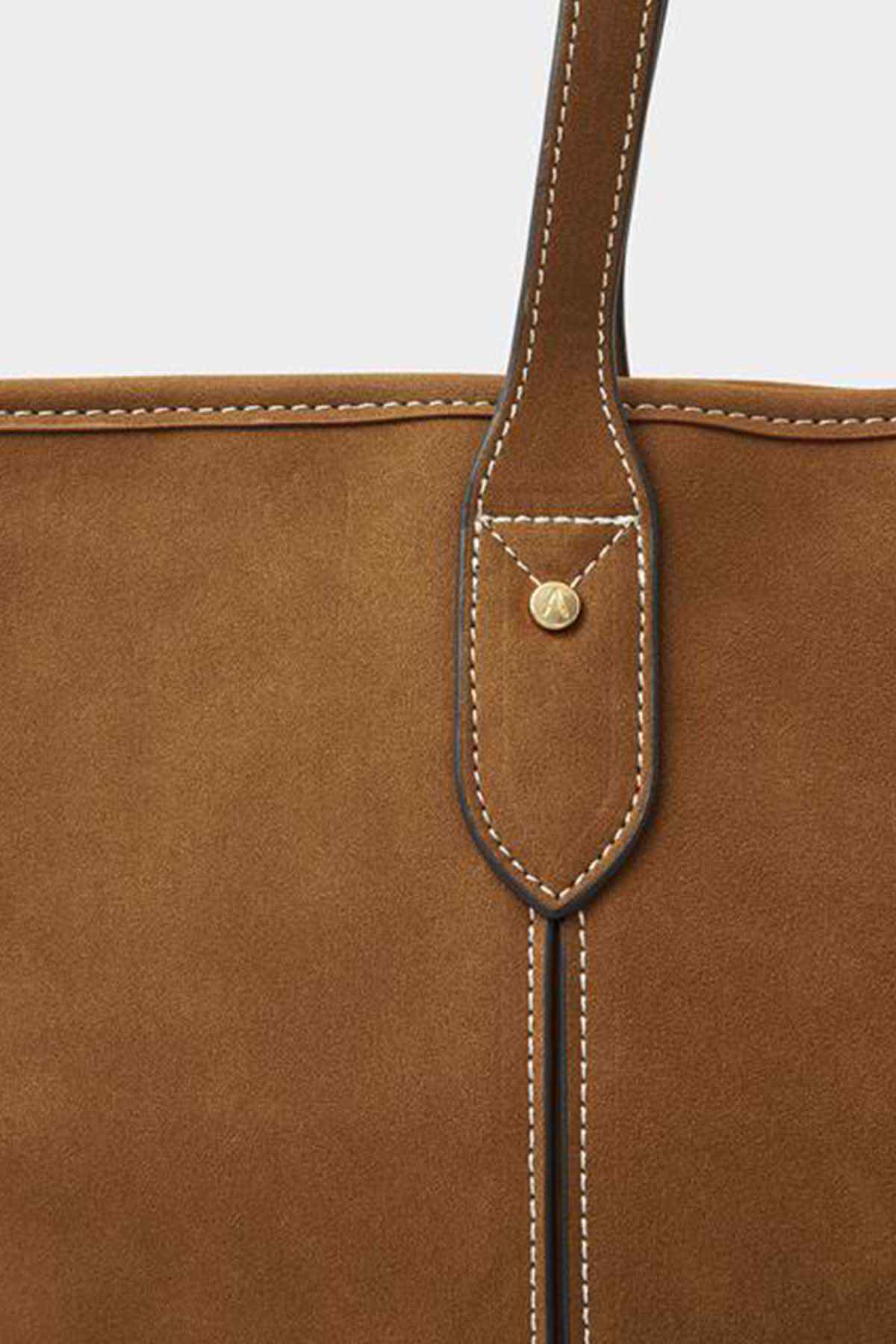 Tan tote bag close-up of handle strap with stitched leather loop and metal snap