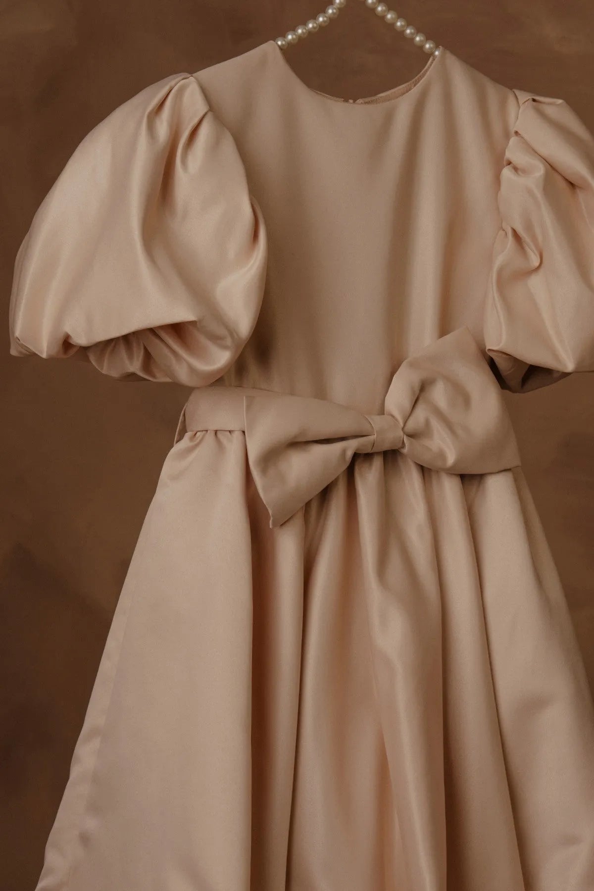 Beige dress close-up: puff sleeves, fitted bodice, and waist bow tie