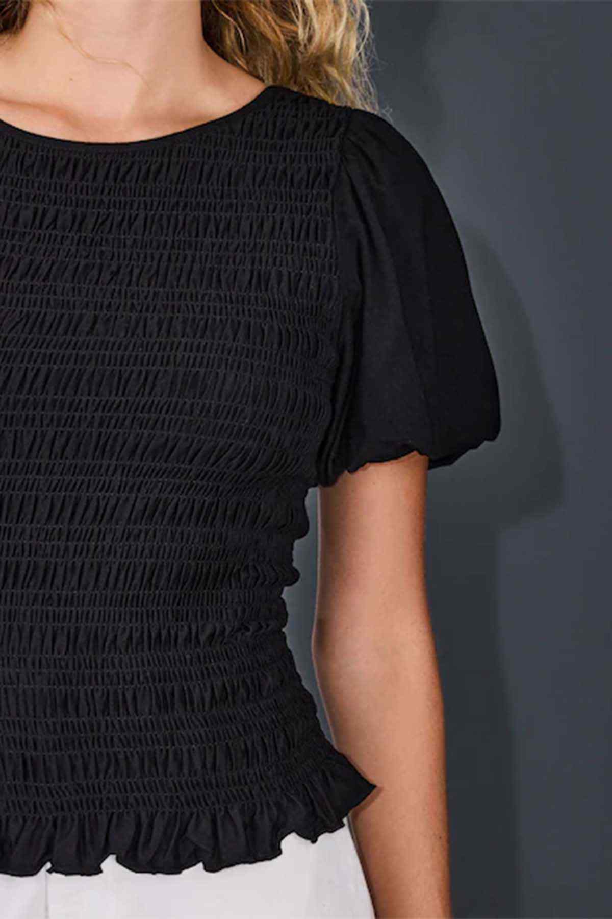 Close-up of black short-sleeve smocked top with gathered texture and ruffle hem