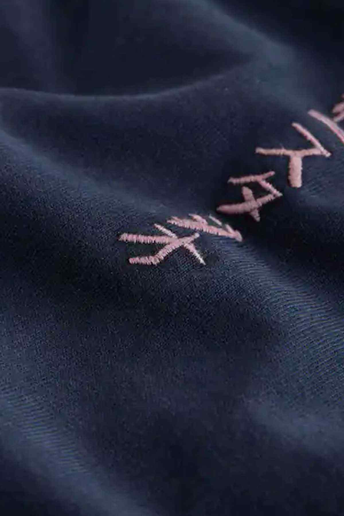 Dark blue T-shirt close-up of light pink stitched embroidery on fabric.