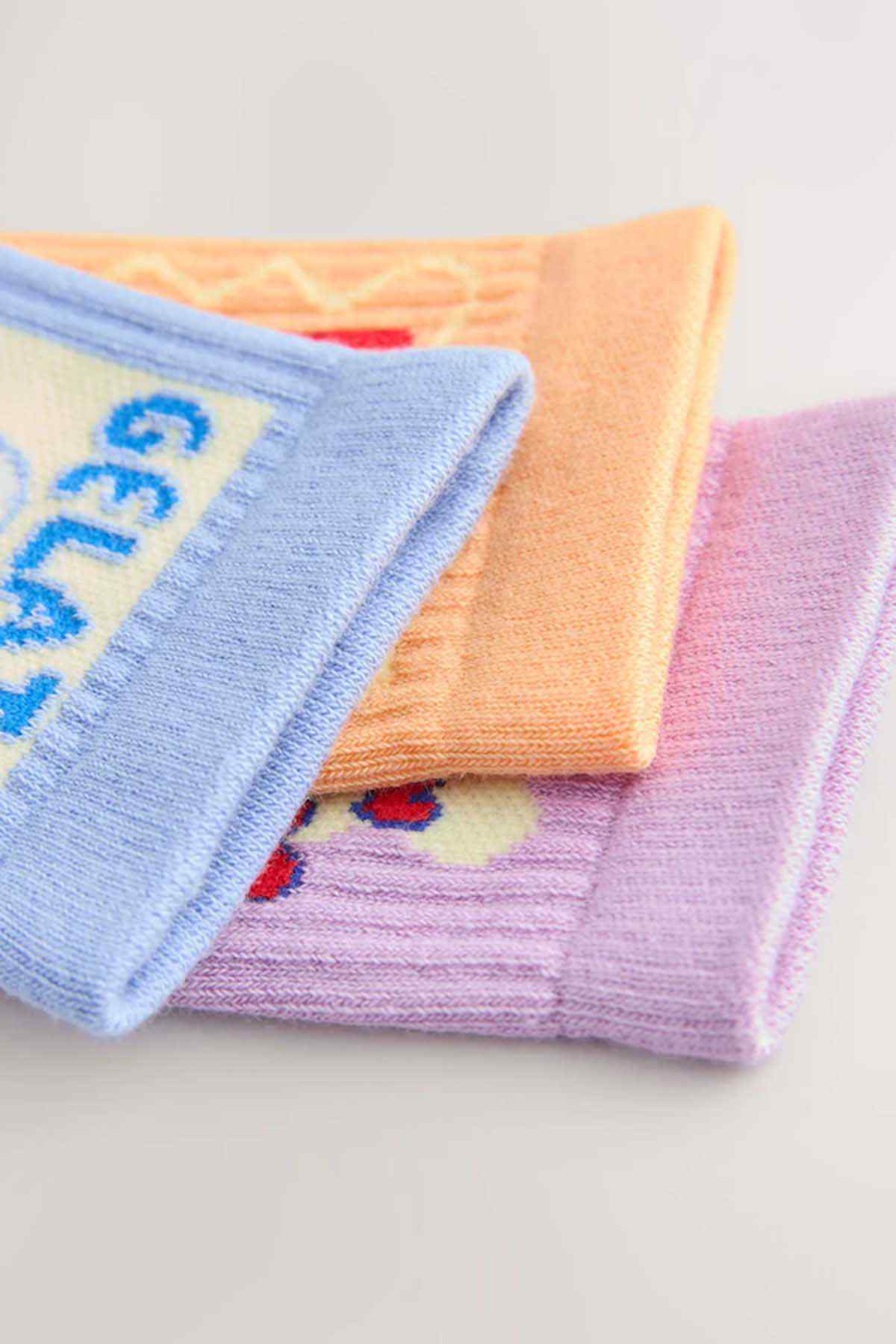 Stack of crew socks with ribbed cuffs in light blue, orange, and lilac knit
