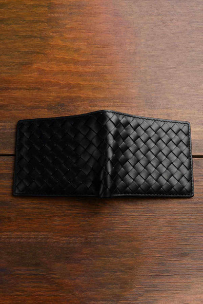 Black woven leather bi-fold wallet with two-tone weave, closed on wooden table