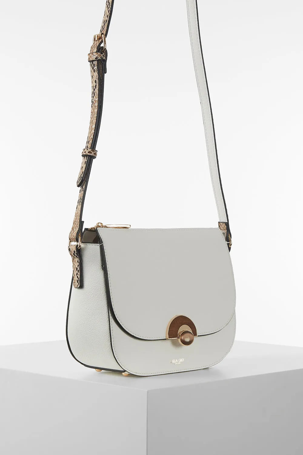 White crossbody bag with flap closure and patterned strap, angled side view