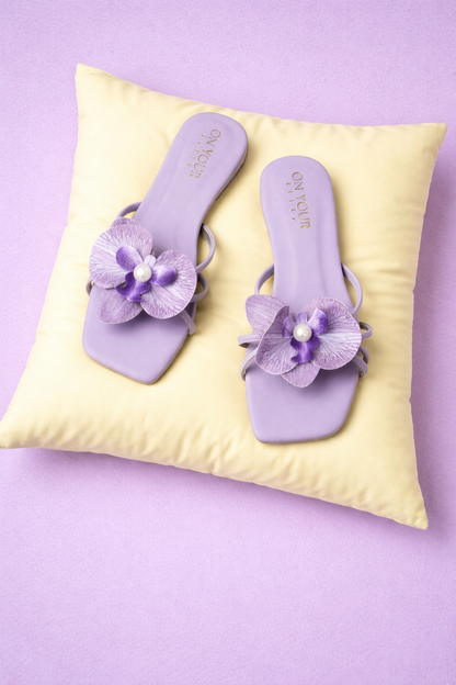 Purple flat slide sandals with flower appliques and pearl accents on pillows