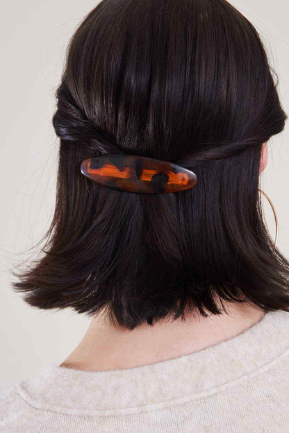 Tortoiseshell orange hair clip on dark hair, curved oval claw style