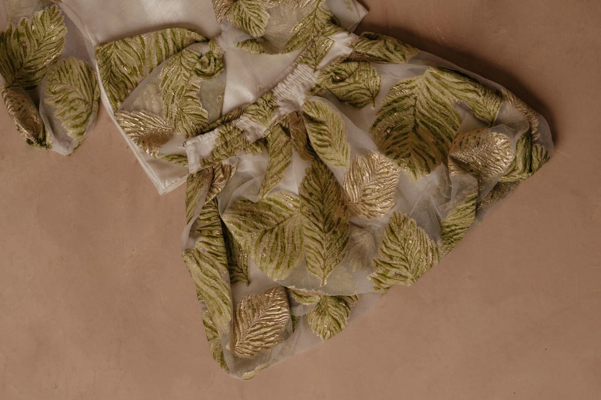 White button-up shirt with gold buttons and green leaf print sleeves
