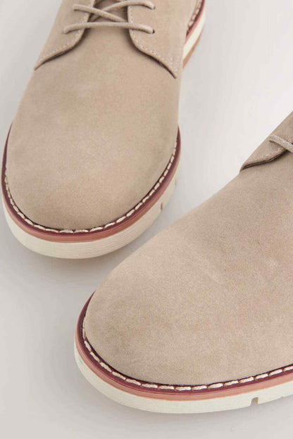 Stone suede lace-up boots close-up, showing red-edged stitching and textured sole