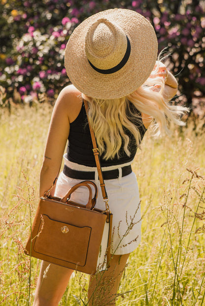 Brown small handbag with shoulder strap and front flap pocket worn crossbody by model.