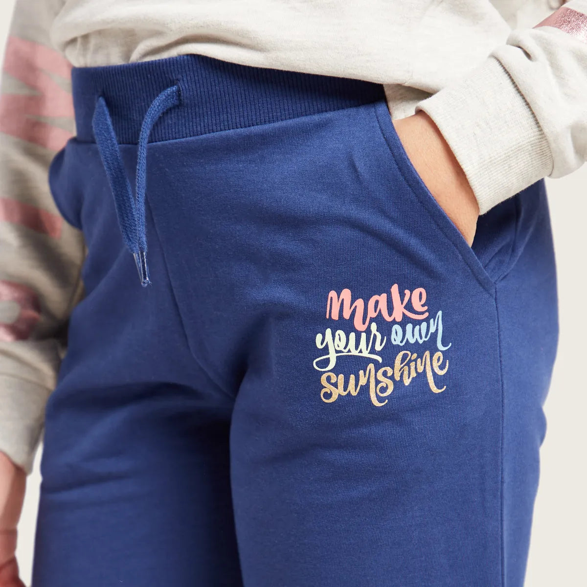 Blue jogger pants close-up with drawstring, side pocket, and 'Make your own sunshine' logo