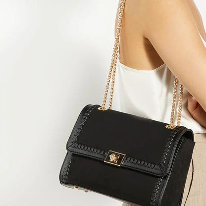 Black crossbody bag with gold chain strap and square clasp, carried at shoulder.