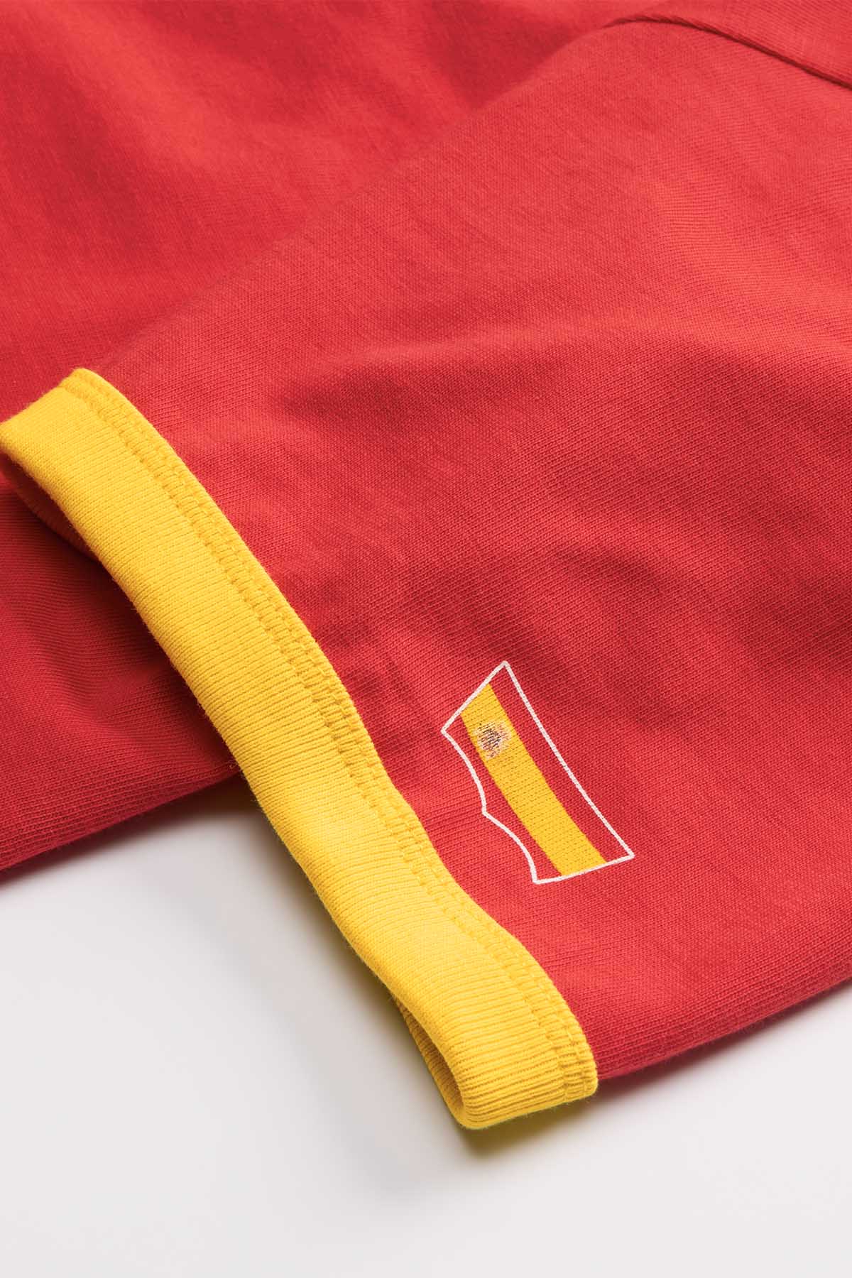 Red T-shirt with yellow ribbed trim and small flag patch