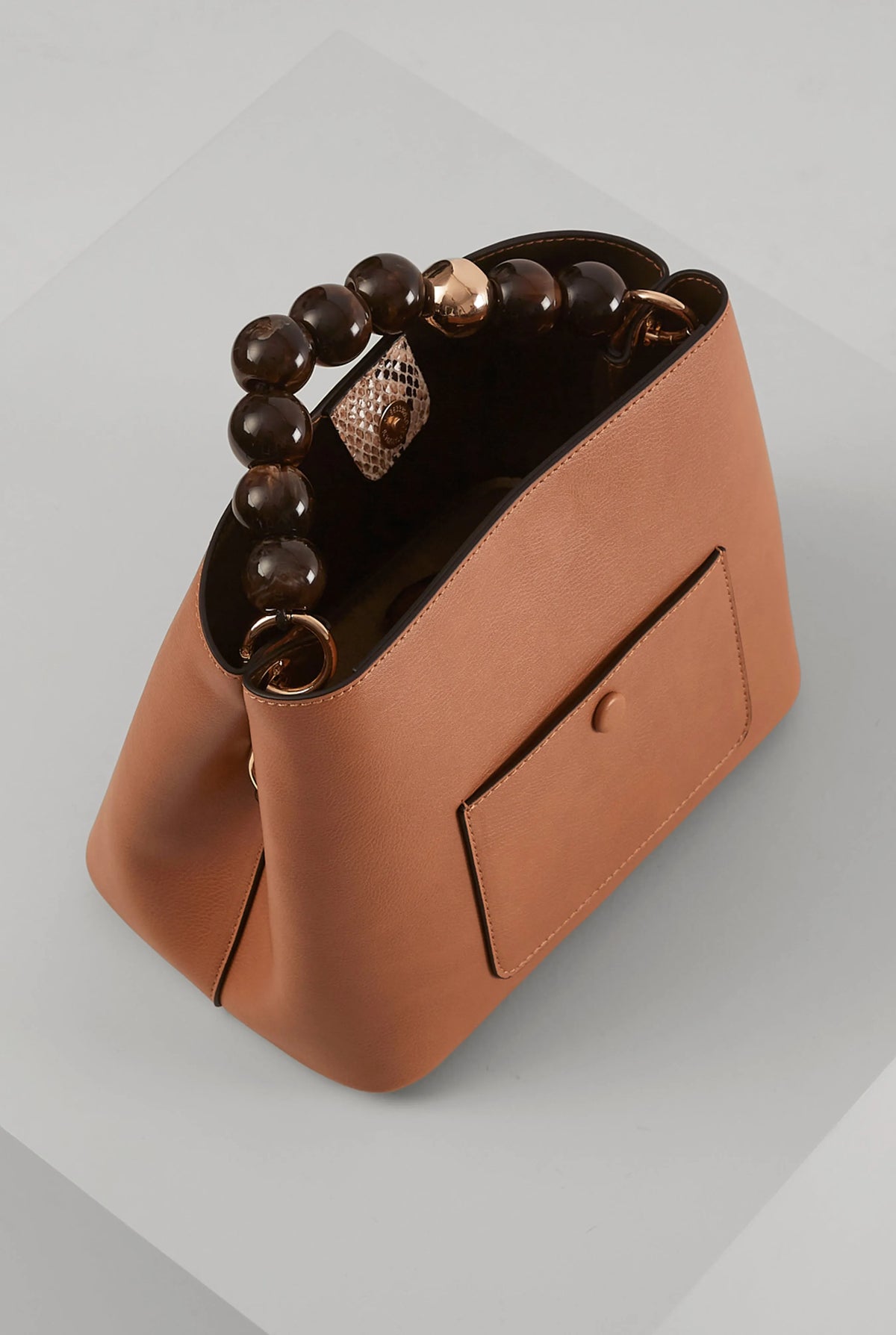 Brown leather bucket handbag with bead handle, side pocket, and top opening