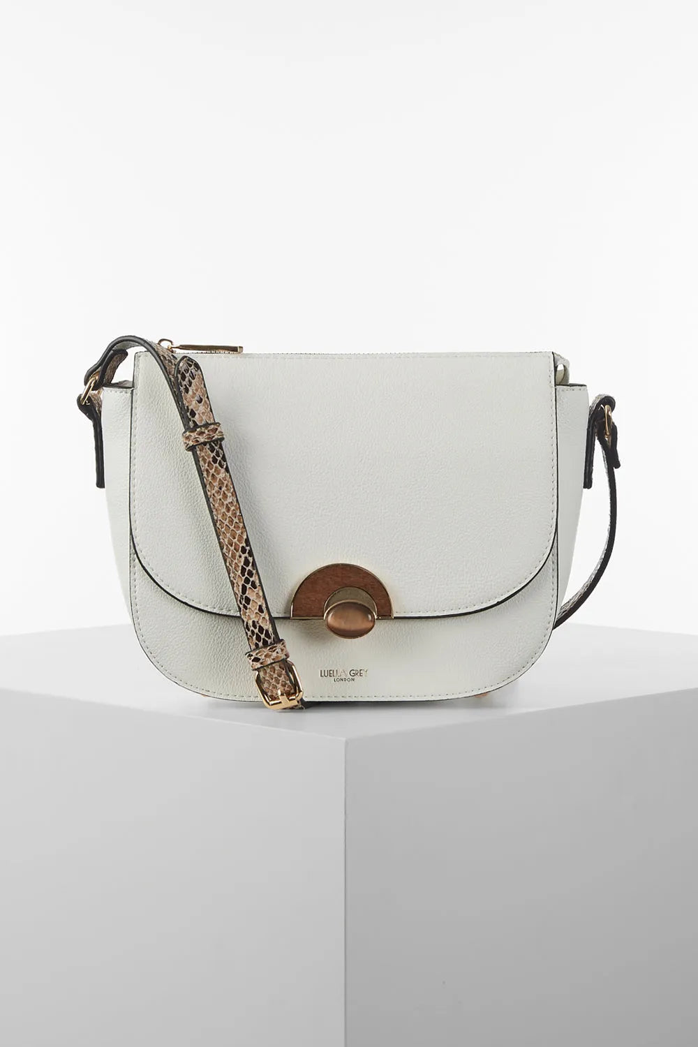 White crossbody saddle bag with flap, round clasp, and patterned shoulder strap