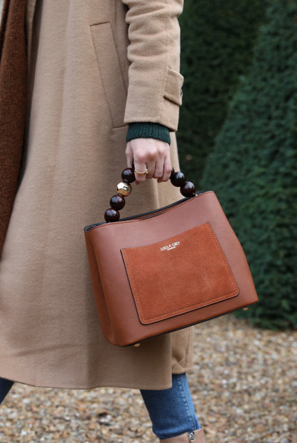 Brown leather mini handbag with beaded handle and front patch pocket, carried by hand.