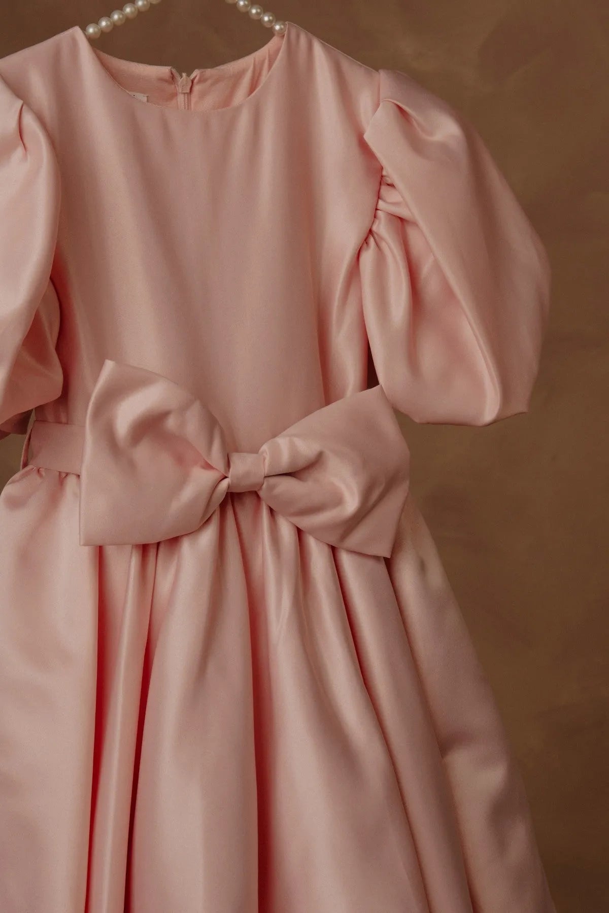 Pink puff-sleeve dress with waist bow and pleated skirt, close-up.