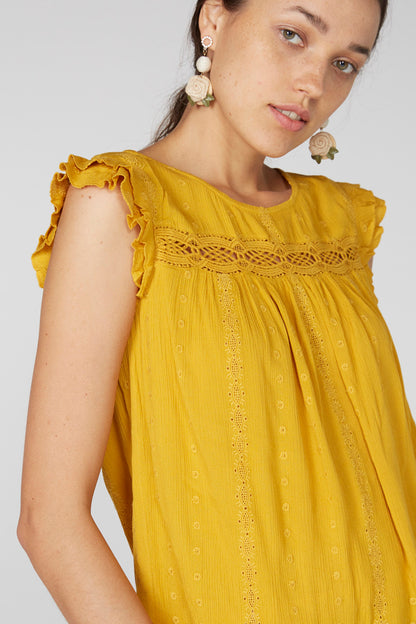 Close-up: yellow sleeveless blouse with ruffled neckline and textured embroidery