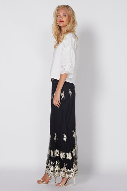 White eyelet blouse with short sleeves and scalloped hem, worn with dark embroidered skirt