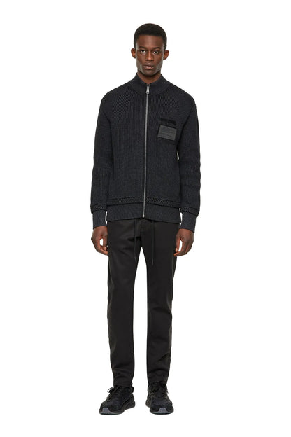 Black knit zip-up jacket with stand collar and chest patch worn with black pants