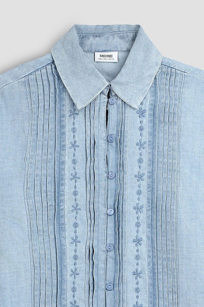 Light blue denim shirt close-up: pointed collar, button placket, embroidered bands