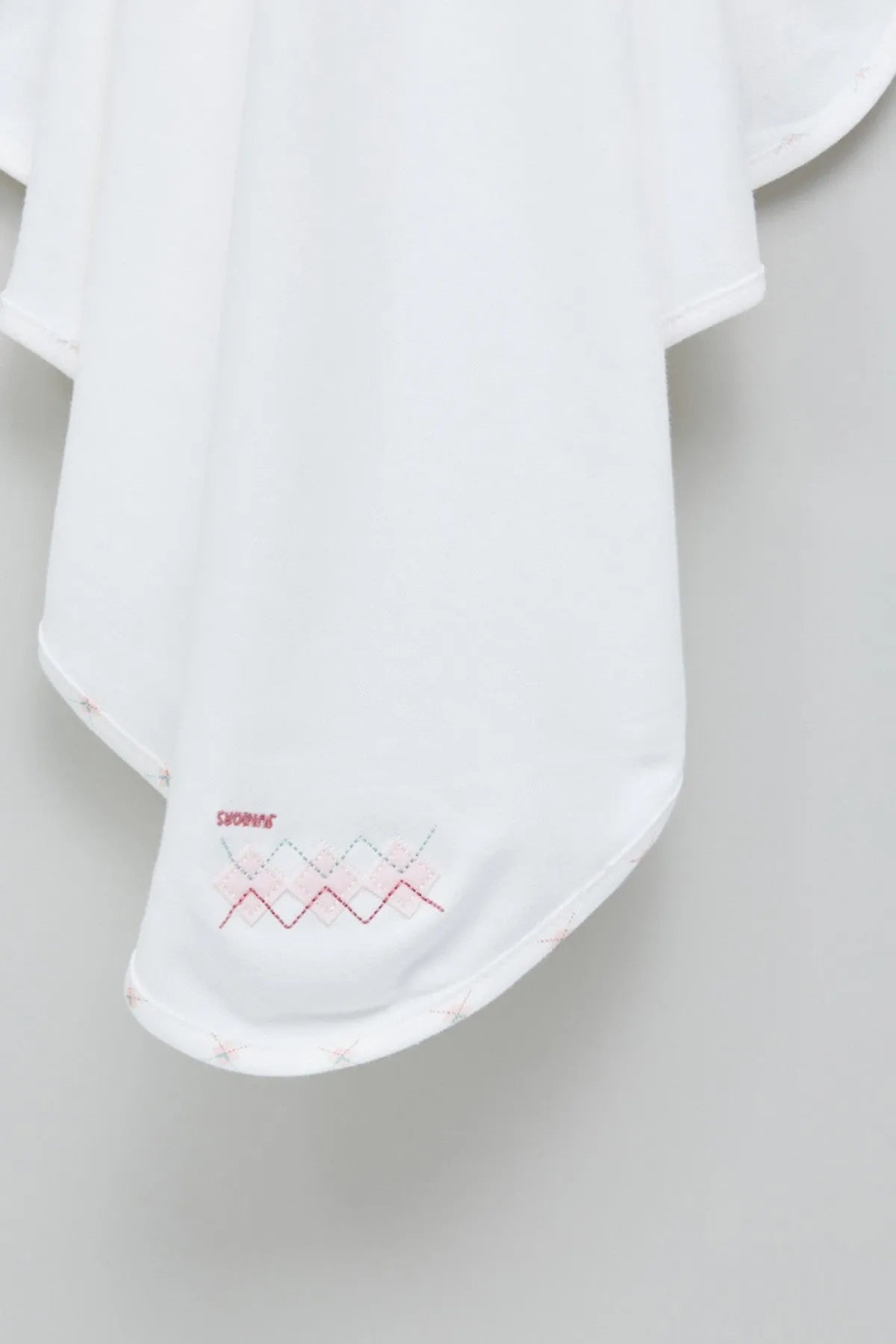 Baby blanket hem with small red and blue geometric embroidery on corner